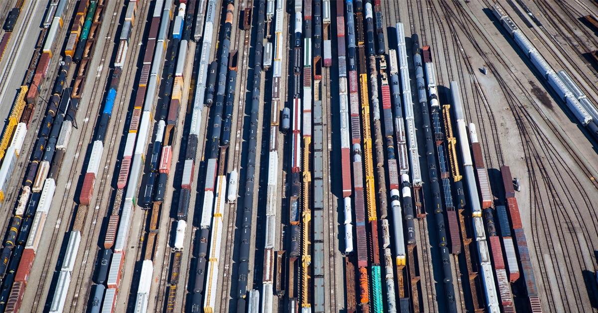 A bustling rail yard with a multitude of train tracks with the yard being filled with a colorful assortment of locomotives and cargo cars of various sizes and shapes. 