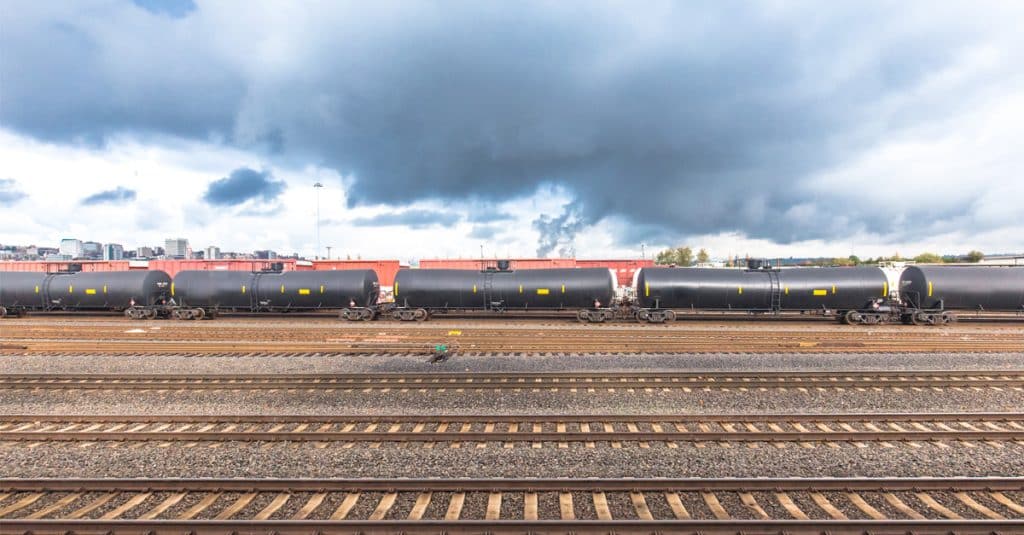 Oil tank and box rail cars against a cloudy sky.