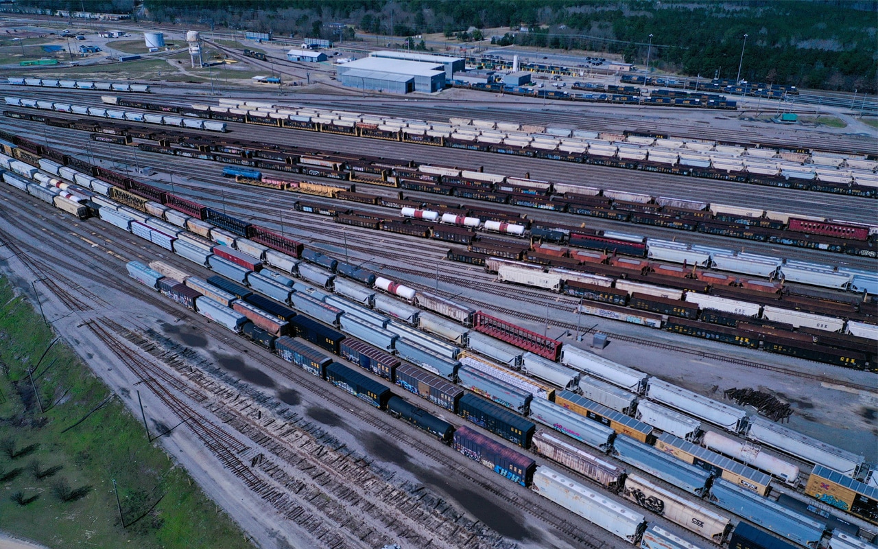 A rail yard beside a factory is filled with freight rail cars.