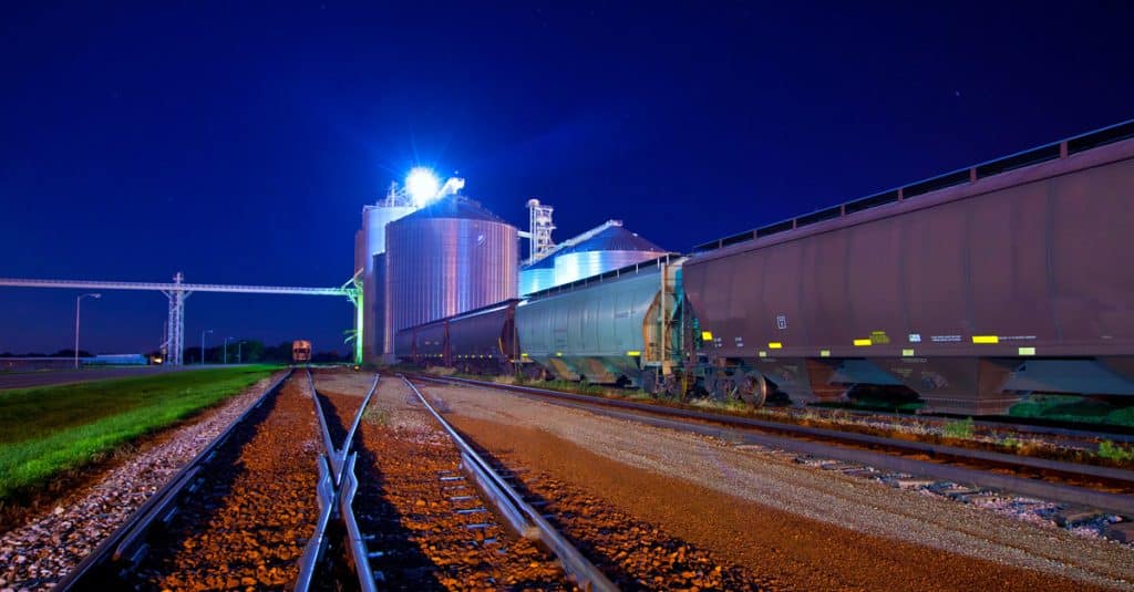 A railyard at night with grain elevators and rail hopper cars.