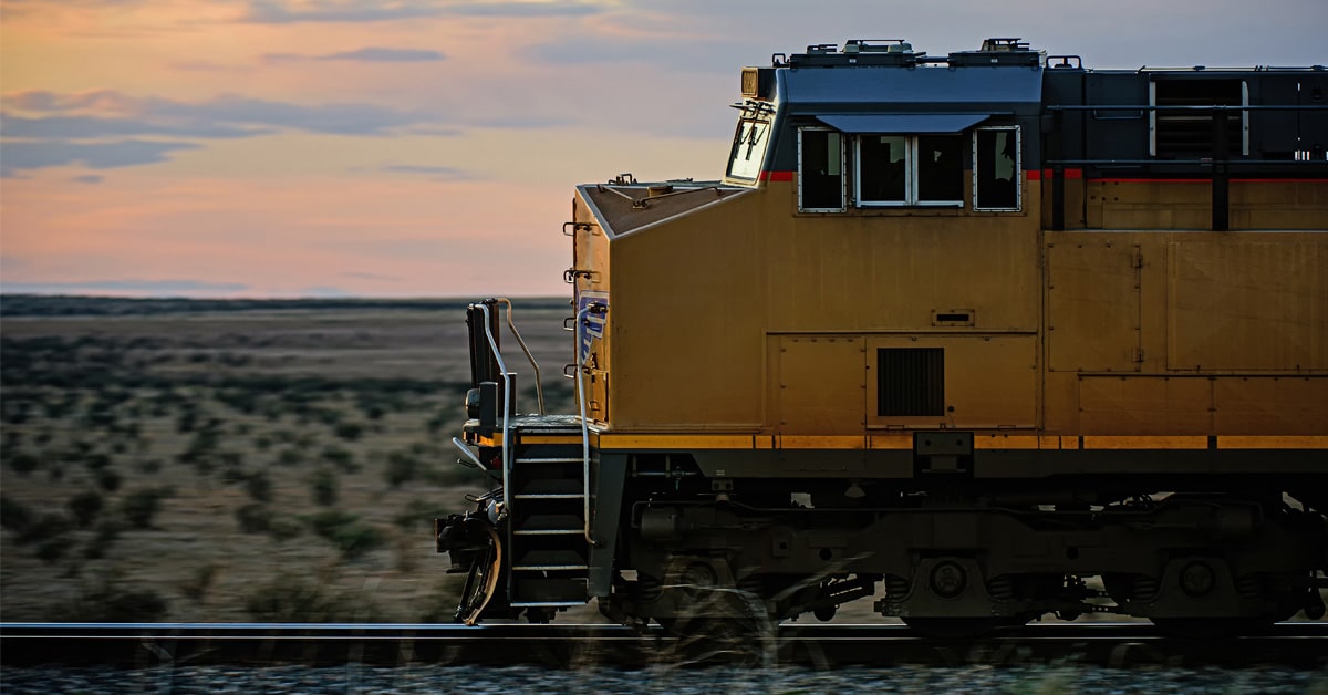 A yellow rail freight engine silhouetted against the sunset in the desert.