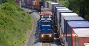 A blue locomotive pulling a short train beside parked container cars.