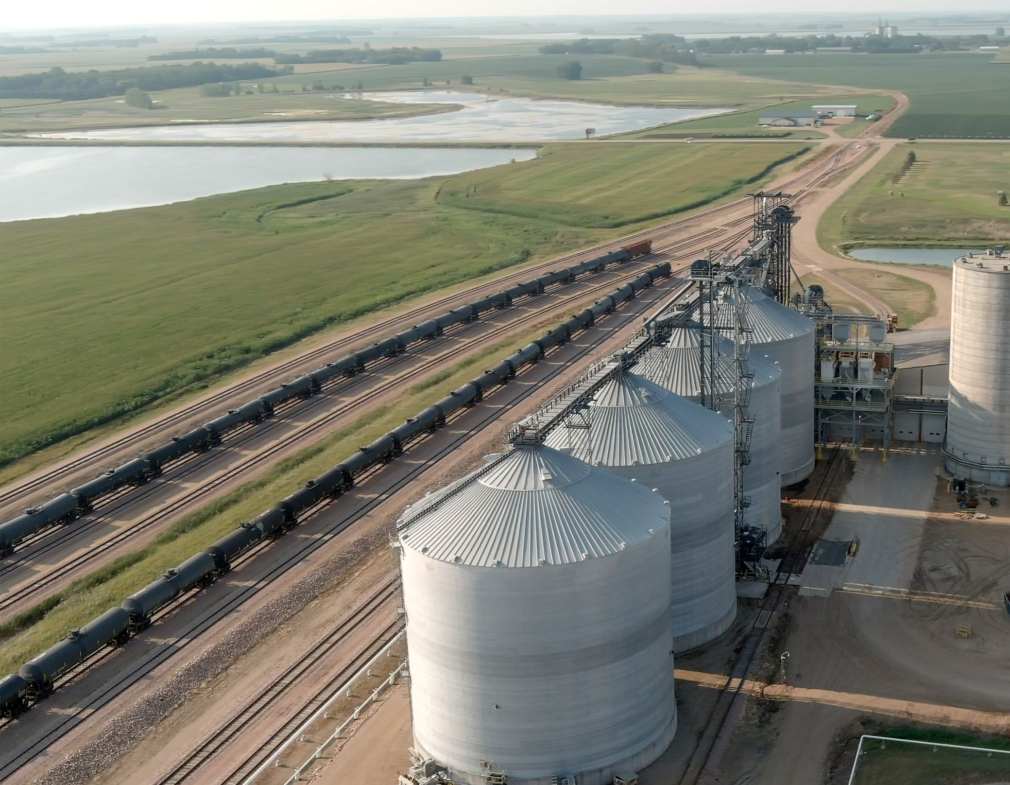 An aerial view of white silos next to two lines of black rail tank cars.